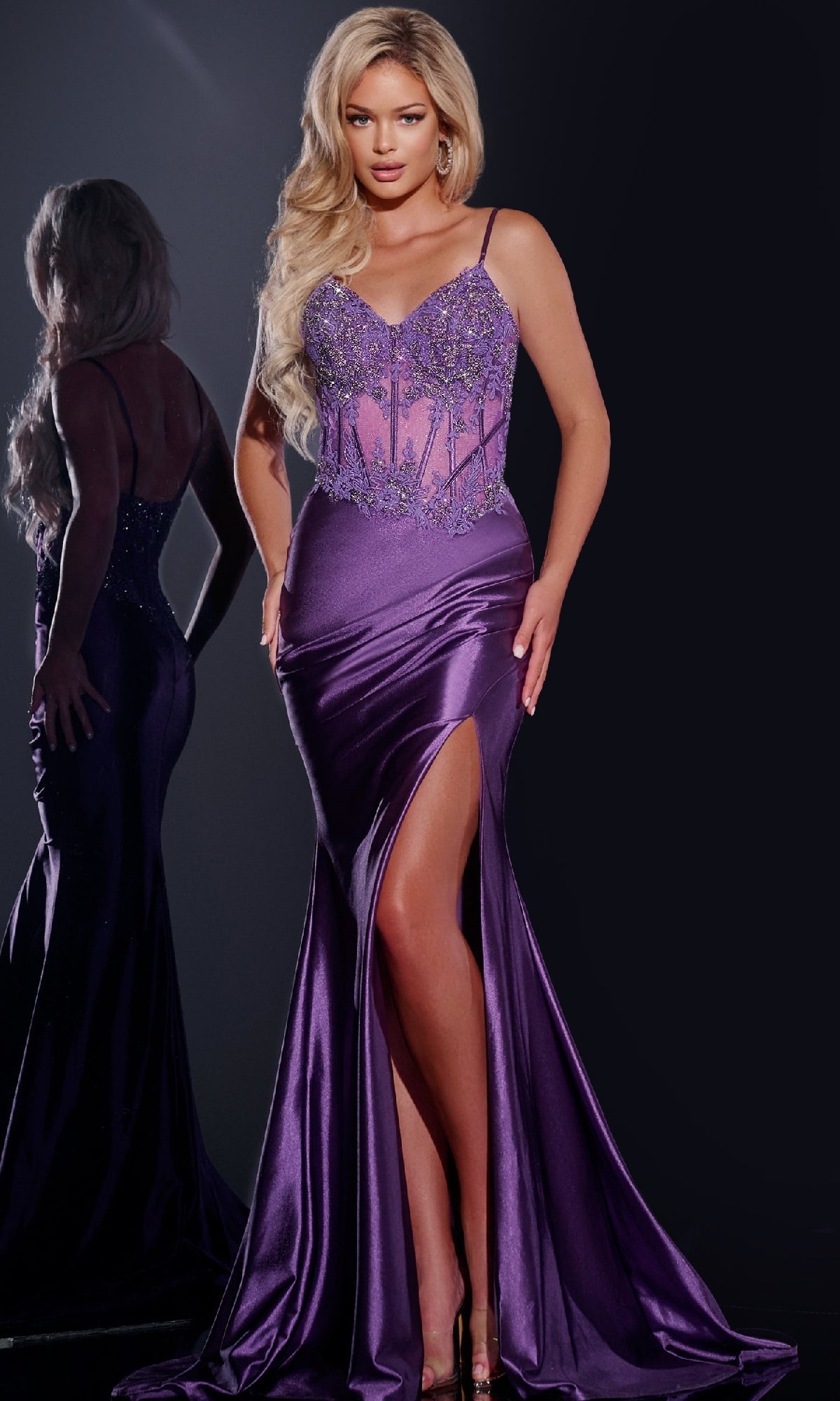 A woman modeling the Sheer-Bodice Long Satin Prom Dress Jovani 42259 with a high slit and beaded bodice stands before a mirror, displaying both the front and back of the elegant satin gown.